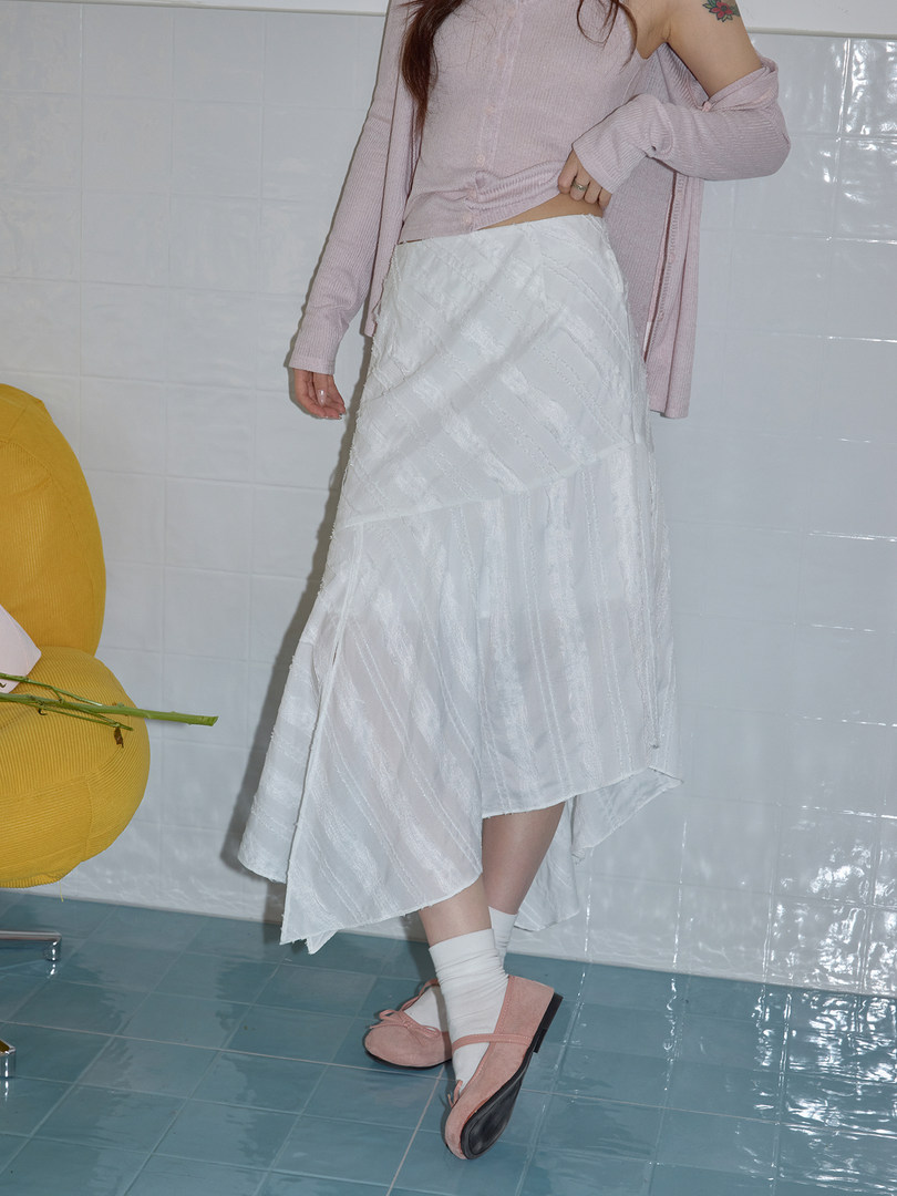 Model wearing a light pink top with a white asymmetrical skirt and pink shoes