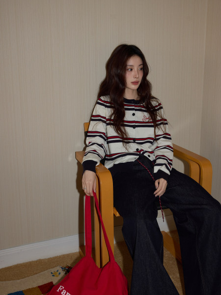 Woman wearing a striped cardigan and black wide-leg jeans while holding a red tote bag