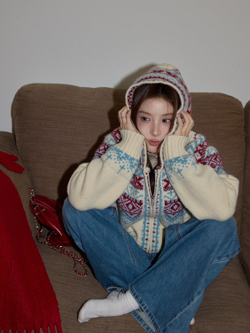 Person wearing a patterned knit hooded sweater and blue jeans while sitting on a couch