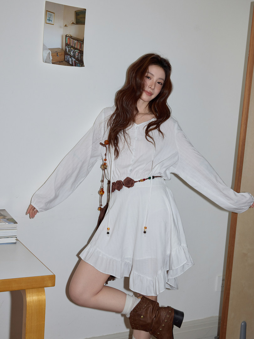 Model wearing a white long-sleeve ruffled mini dress with a beaded waist belt