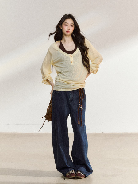Model wearing a pale yellow sheer long-sleeve top with dark jeans