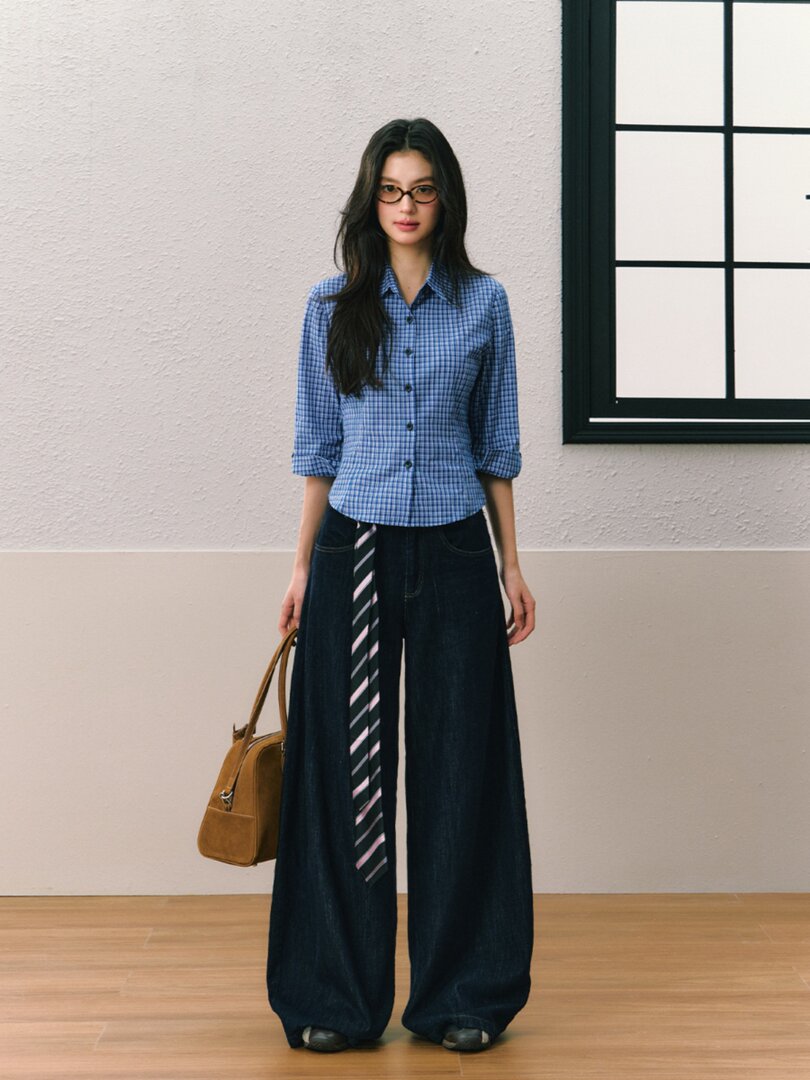 Model wearing a blue checkered button-up blouse with wide-leg dark pants and a handbag