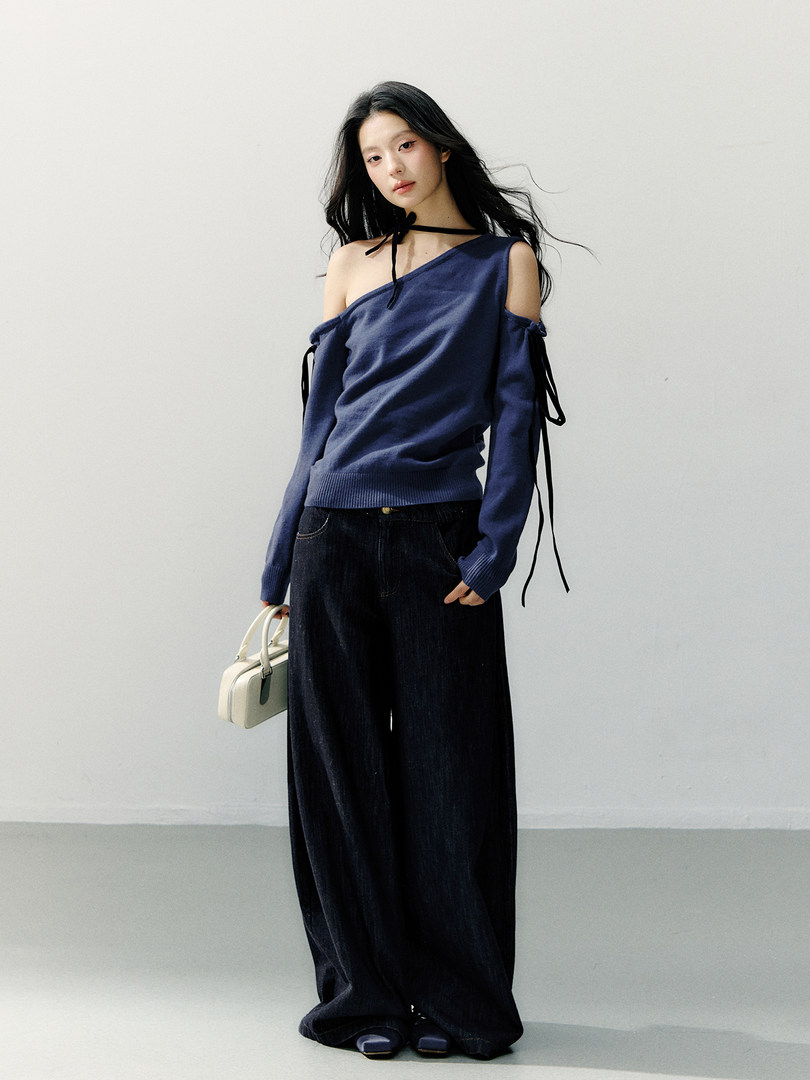 Model wearing a navy off-shoulder sweater with wide-leg dark pants and a small handbag