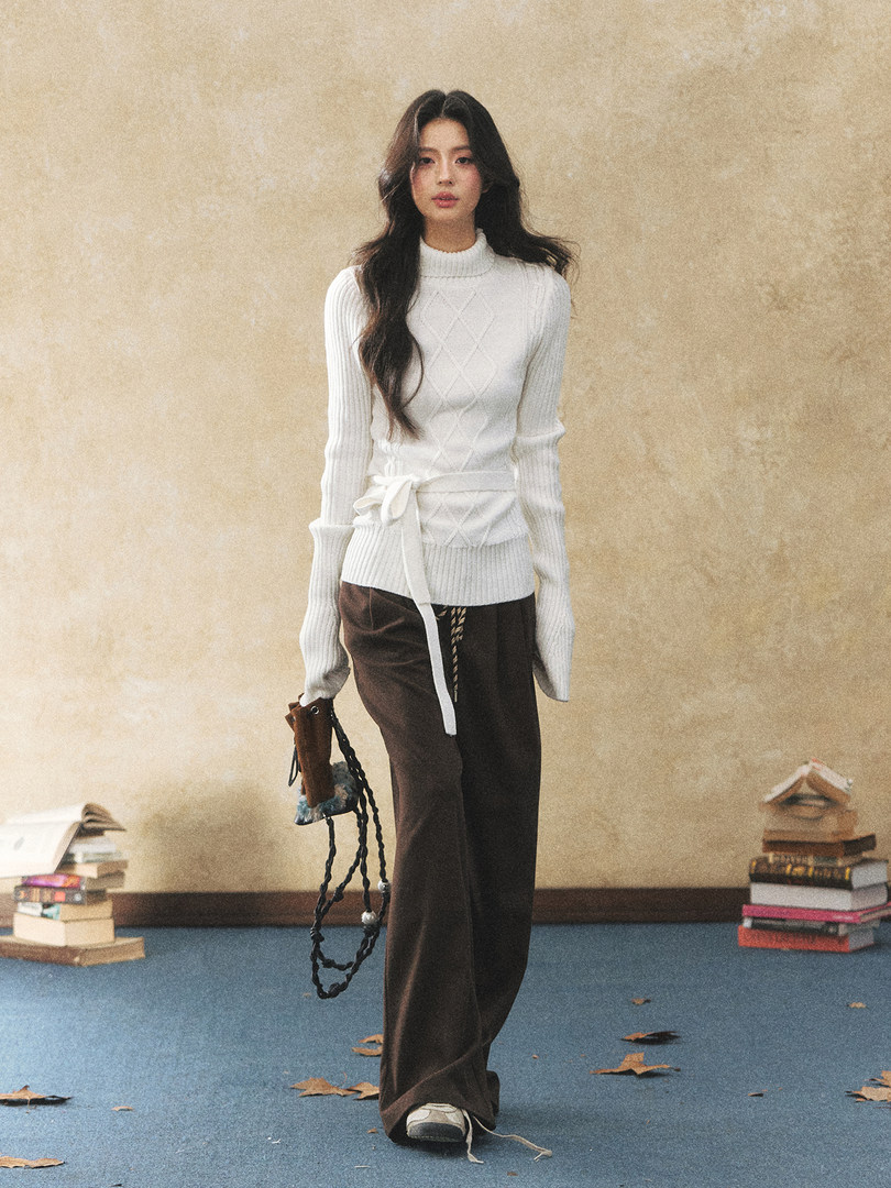 Model wearing a white ribbed knit sweater with a tied waist and brown pants