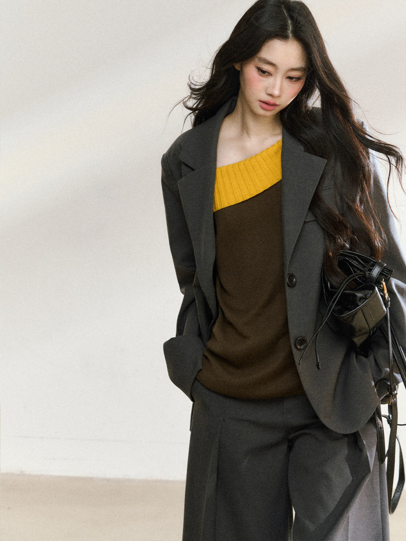 Model wearing a dark gray blazer and trousers with a yellow and brown knit top and black handbag