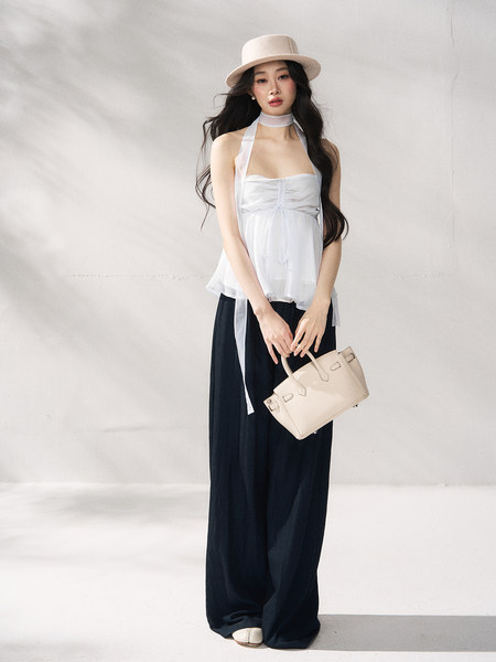 Model wearing a white halter top and black wide-leg pants with a beige hat and handbag