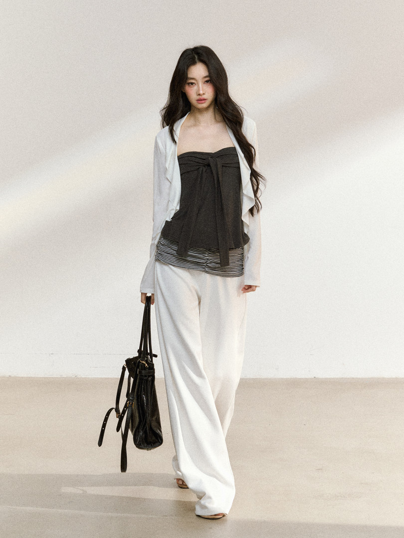 Woman modeling a layered black and white fashion outfit with wide-leg pants and a handbag