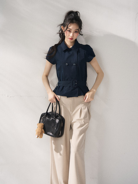 Model wearing a navy belted short-sleeve blouse with beige trousers and carrying a black handbag