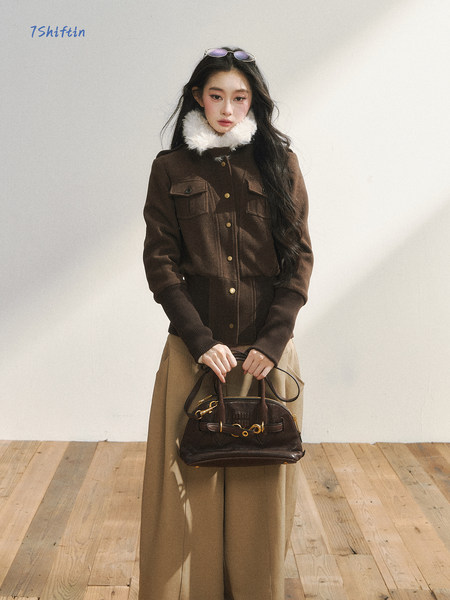 Model wearing a brown jacket with a white fur collar and holding a dark handbag