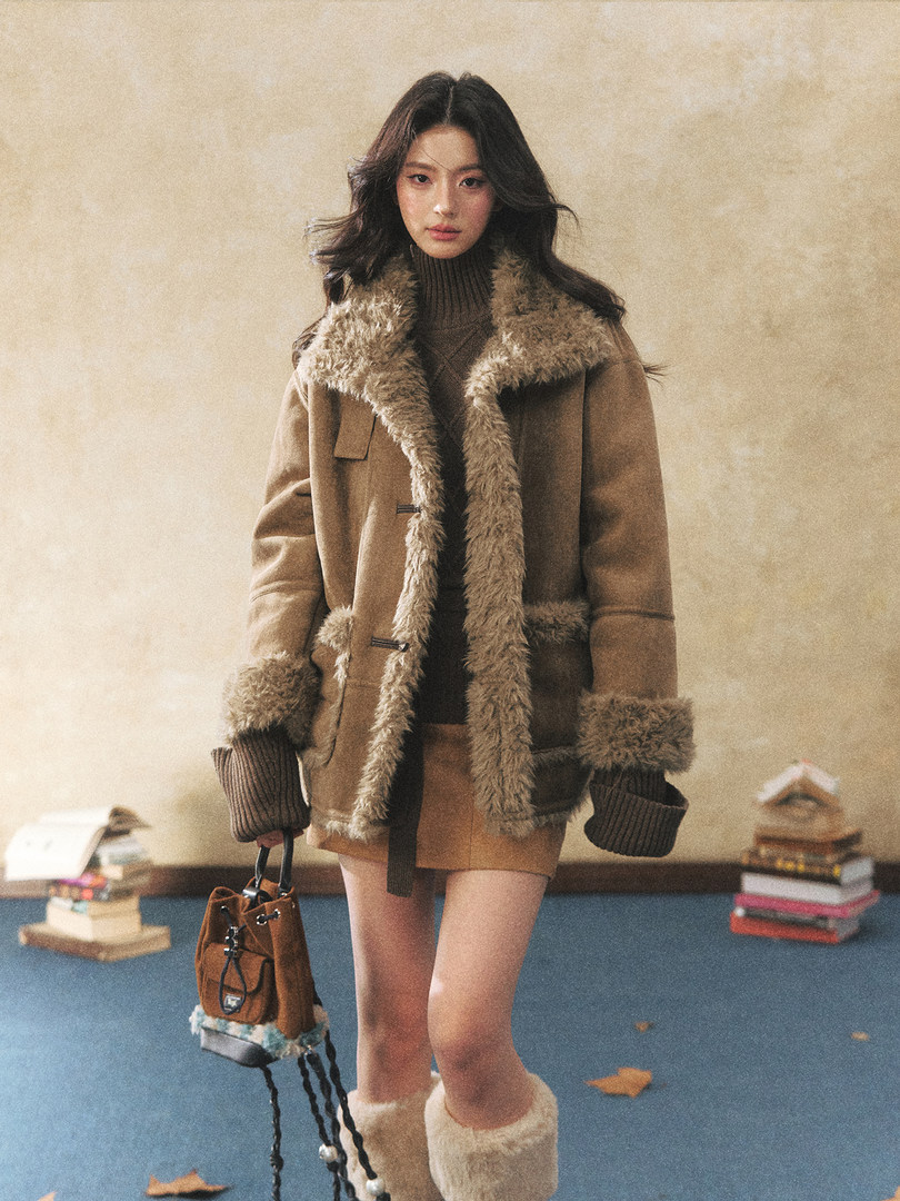 Model wearing a tan shearling coat with fur trim and holding a brown bag