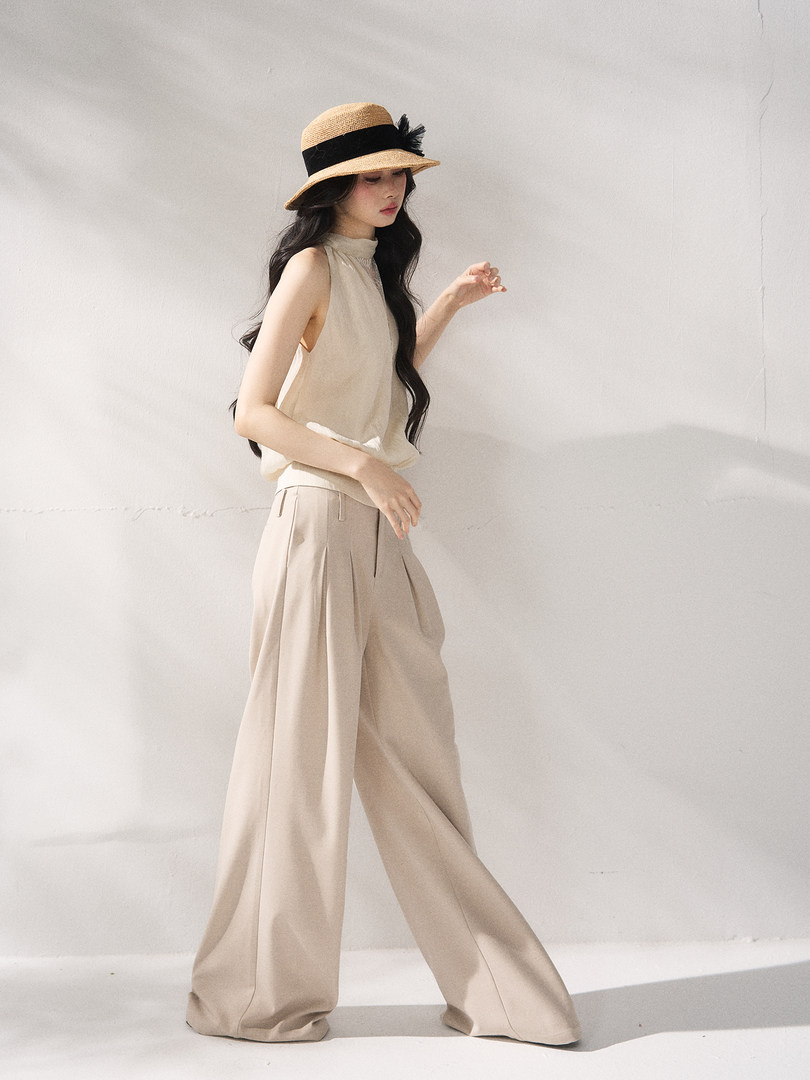 Model wearing a beige sleeveless top and wide-leg trousers with a straw hat