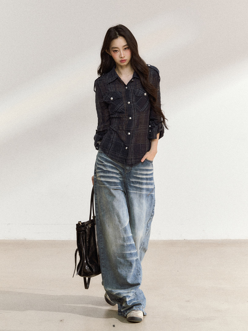 Model wearing a dark plaid button-up shirt with baggy faded jeans and a black bag