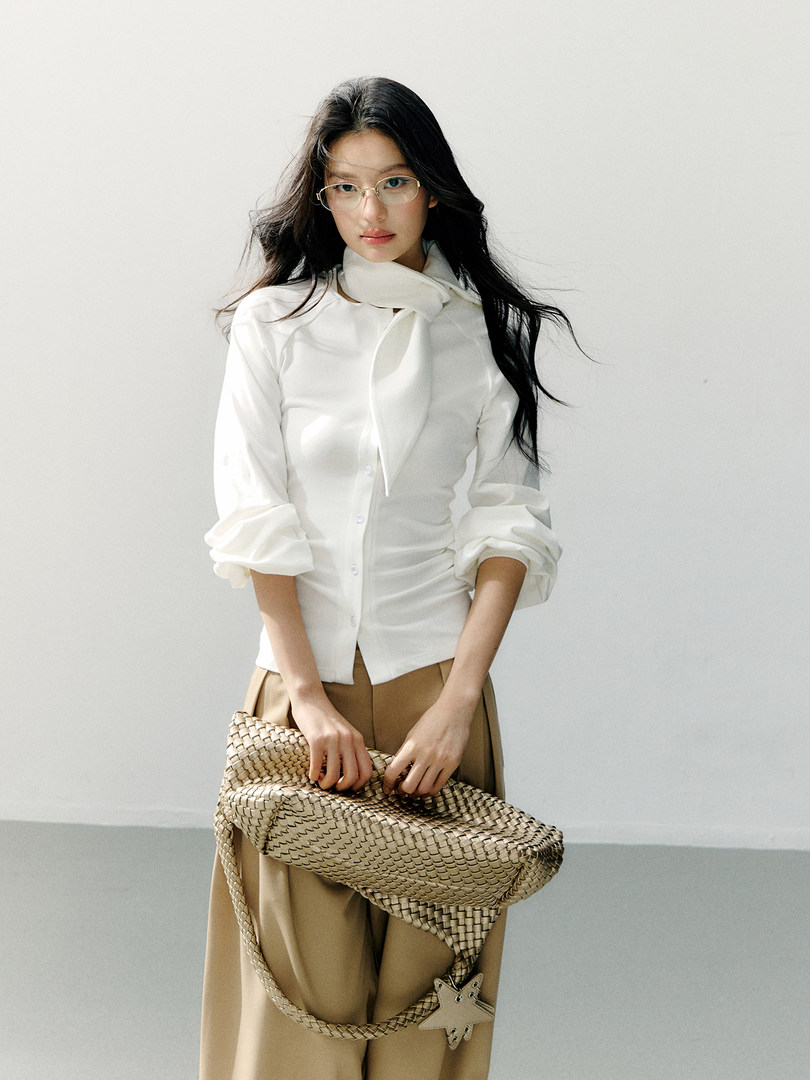 Woman wearing a white blouse and holding a woven handbag