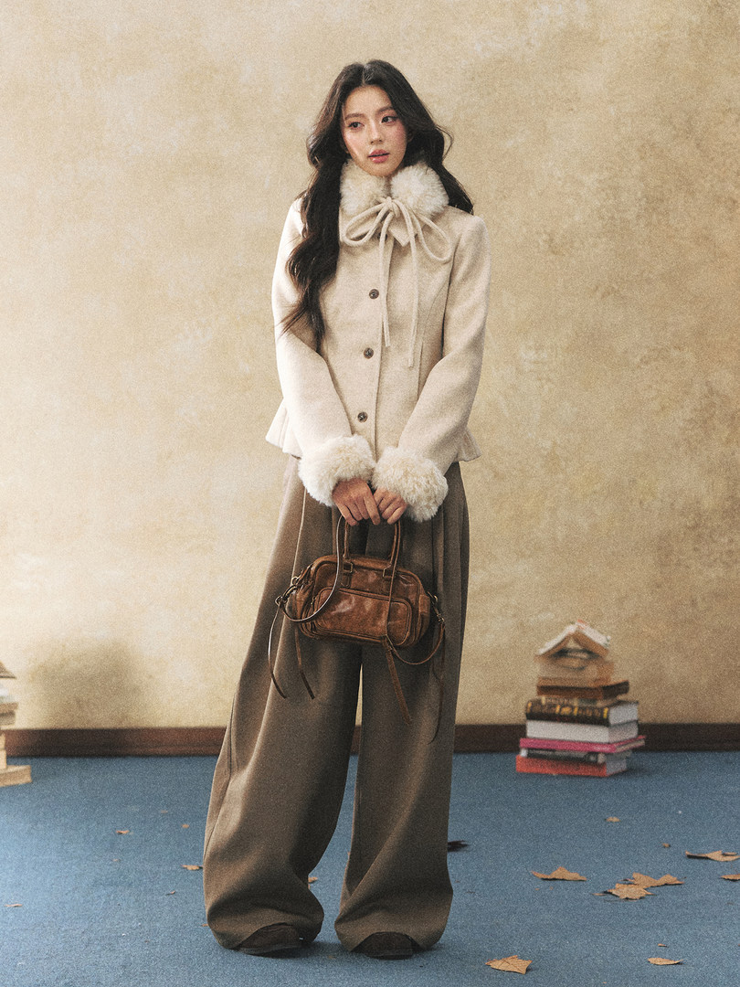 Model wearing a cream fur-trimmed winter coat with wide-leg pants and holding a brown handbag