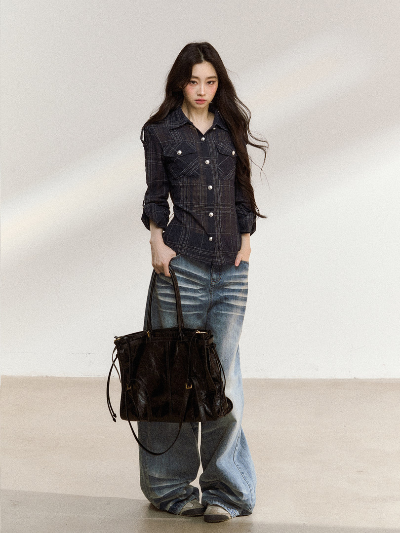 Model wearing a dark plaid button-up shirt with wide-leg jeans and a black tote bag