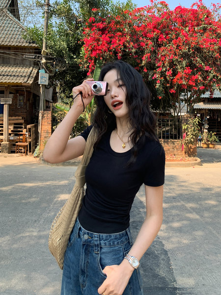 Woman wearing a black fitted T-shirt and blue jeans with a woven tote bag outdoors