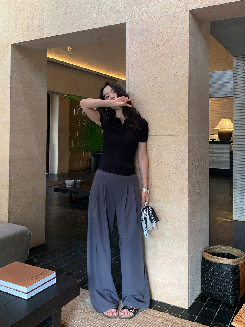 Woman wearing a black fitted top and gray wide-leg pants in an indoor setting