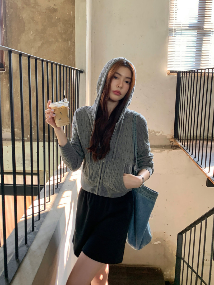 Woman wearing a gray hooded cable-knit sweater and black skirt