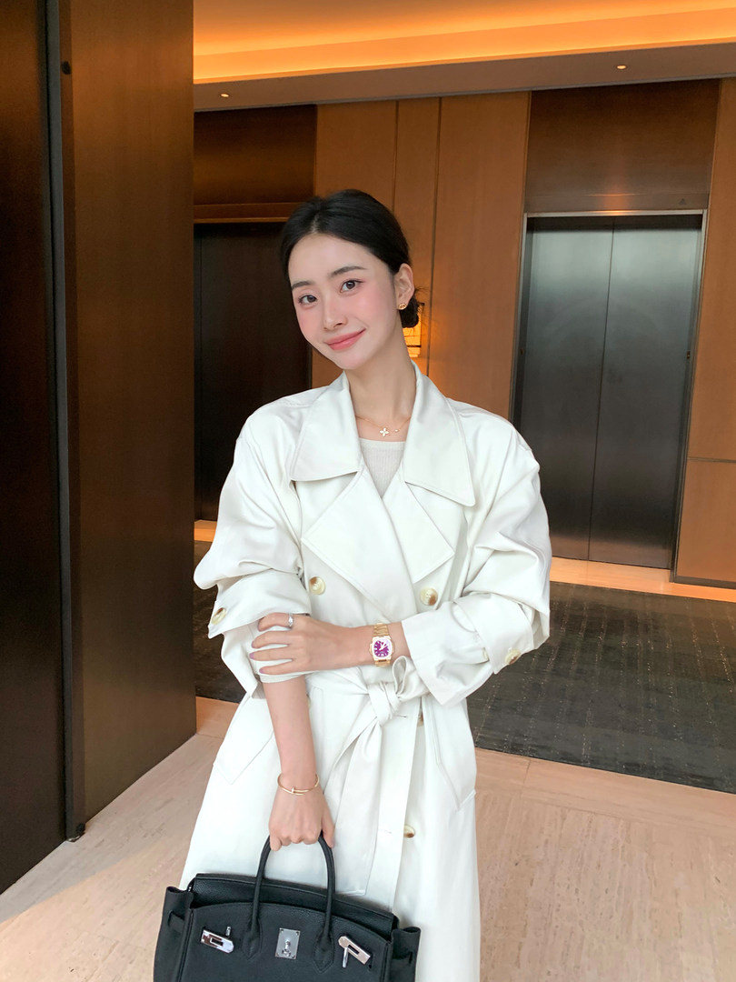 Woman wearing a white trench coat and holding a black handbag