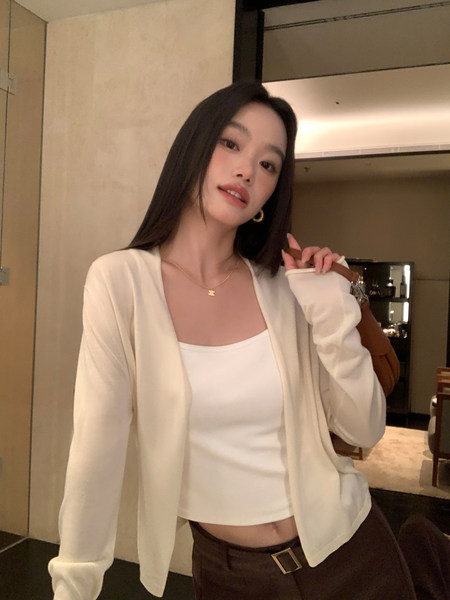 Woman wearing a cream cardigan over a white tank top with brown pants in an indoor mirror selfie