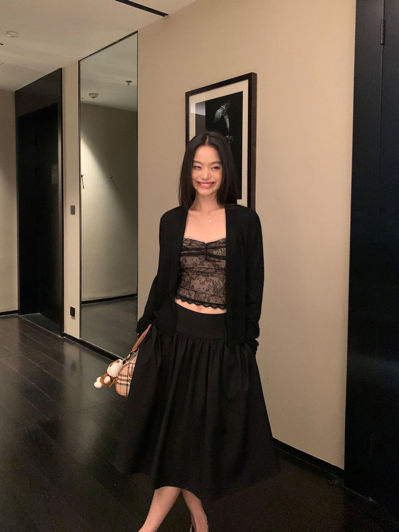 Woman wearing a black lace top, cardigan, and long skirt in a stylish indoor outfit photo