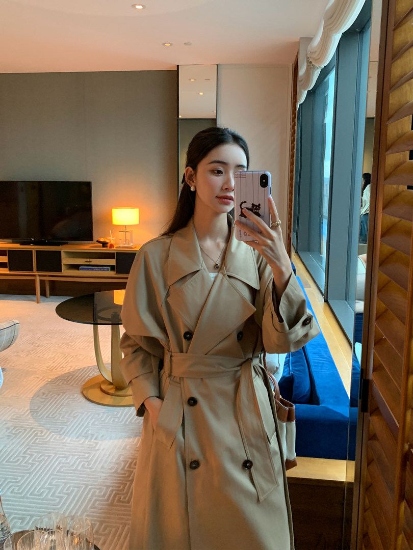Woman wearing a beige trench coat in a mirror selfie