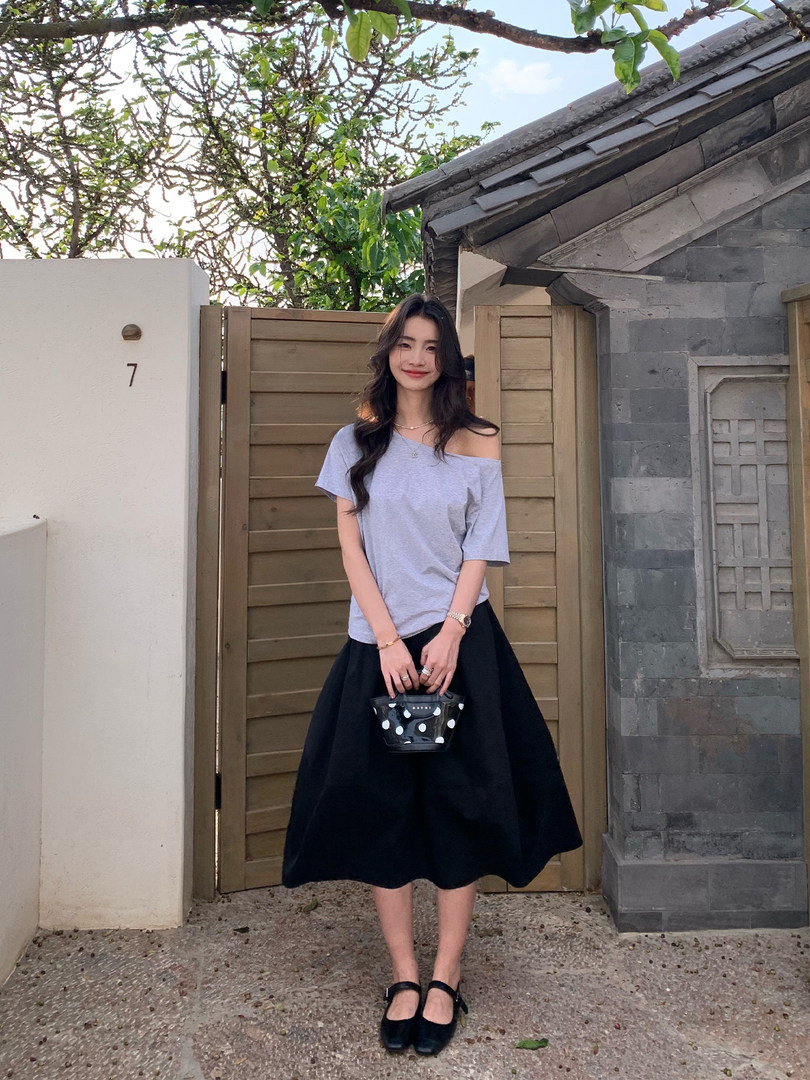 Woman wearing a light gray off-shoulder top with a black midi skirt and small polka dot handbag