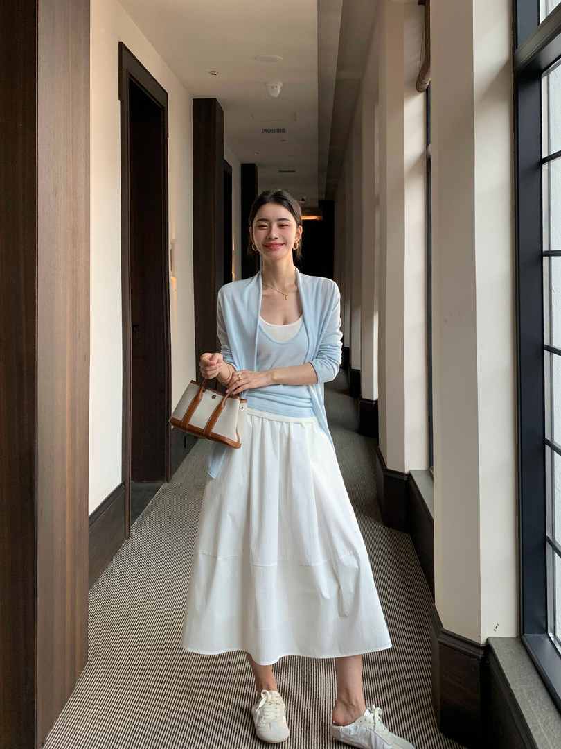 Woman wearing a light blue cardigan and white skirt with sneakers and a small handbag