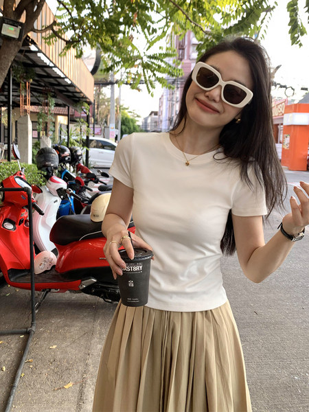 Woman wearing a white fitted short-sleeve top with a beige pleated skirt outdoors