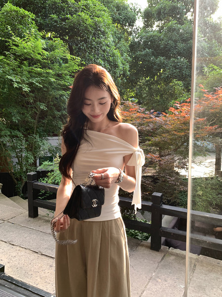 Woman wearing a cream off-shoulder top and beige wide-leg pants holding a black handbag outdoors