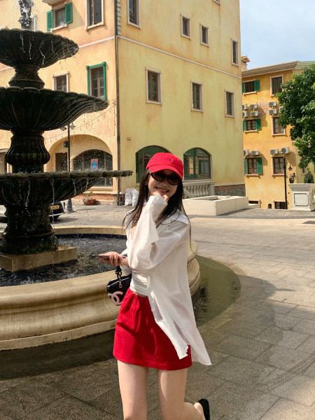 Woman wearing a red skirt, white top, and red cap outdoors by a fountain