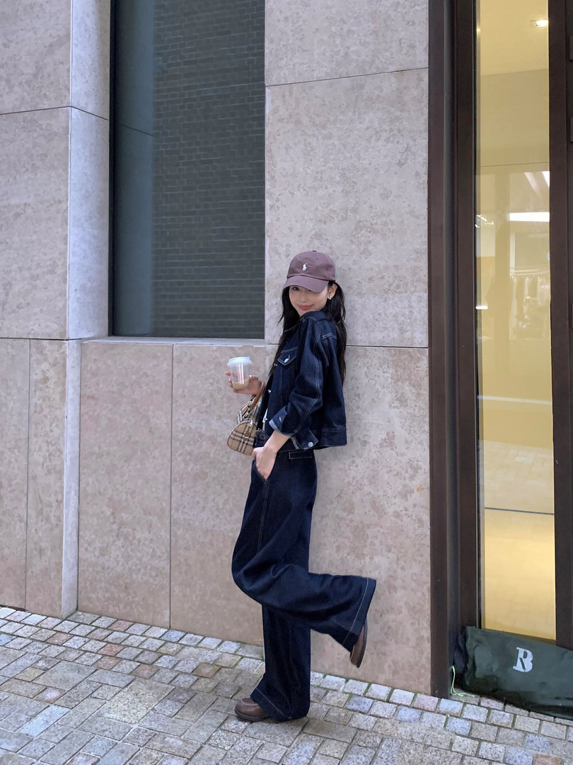 Woman wearing a dark denim outfit with cap and loafers on a city street