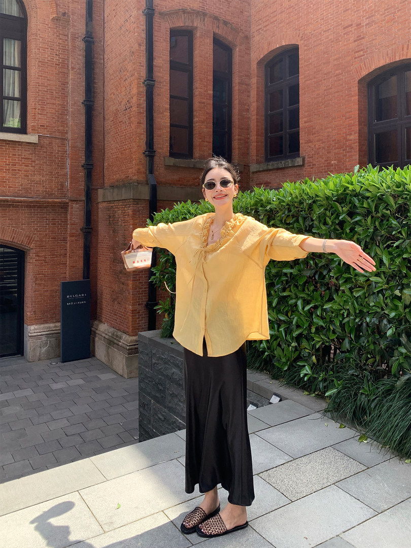 Woman wearing a yellow ruffled blouse with black wide-leg pants and woven slip-on shoes outdoors