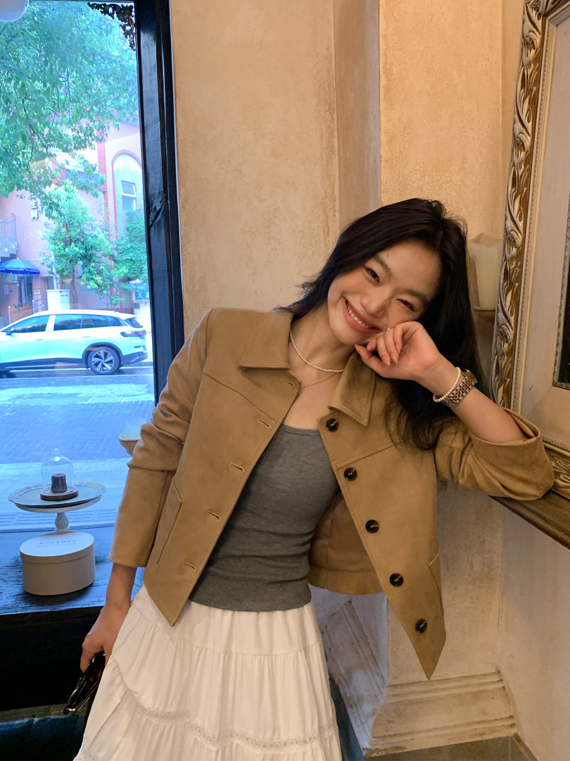 Woman wearing a tan cropped jacket with a gray top and white skirt