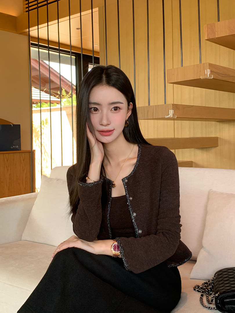 Woman wearing a dark brown cardigan over a black outfit while seated indoors