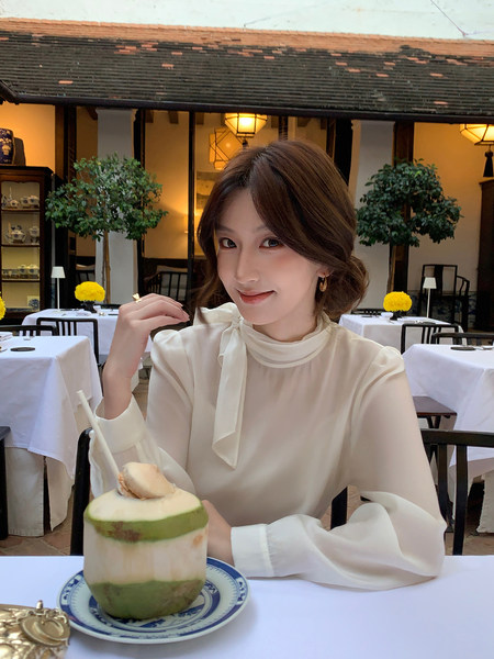 Woman wearing a cream sheer blouse with a neck tie detail