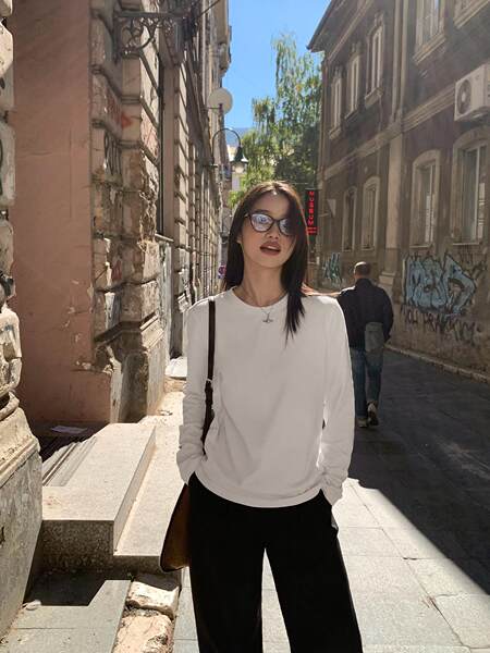 Woman wearing a white long-sleeve top and black pants outdoors in a street setting