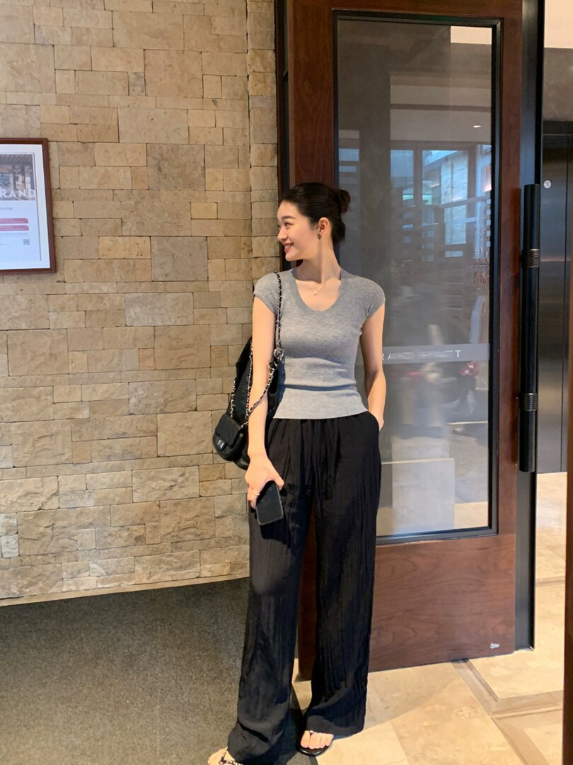 Woman wearing a gray fitted top with black wide-leg pants and a black shoulder bag