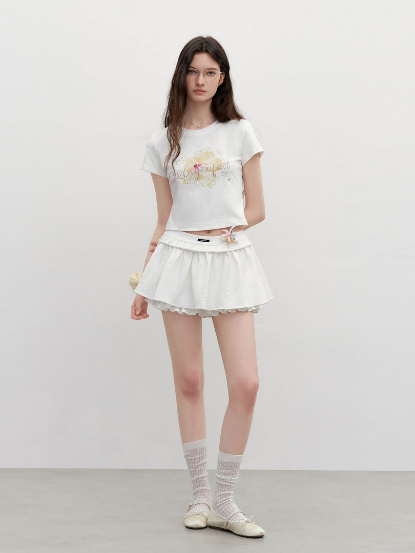 Model wearing a white cropped graphic tee with a white pleated mini skirt, socks, and flats