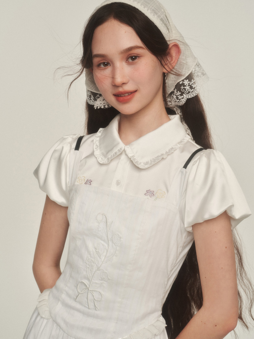 Model wearing a white embroidered dress with puff sleeves and lace headscarf