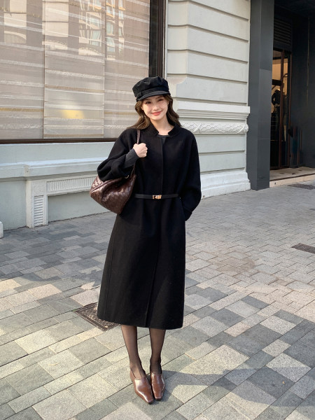 Woman wearing a black belted long coat with matching hat and brown handbag