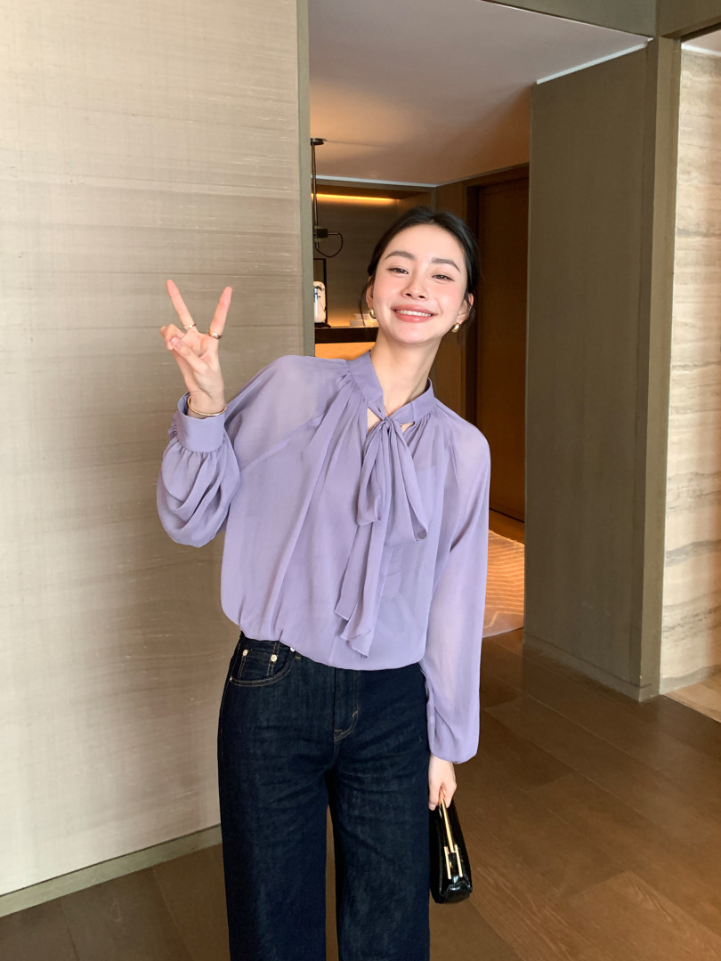 Woman wearing a lavender tie-neck blouse and dark jeans