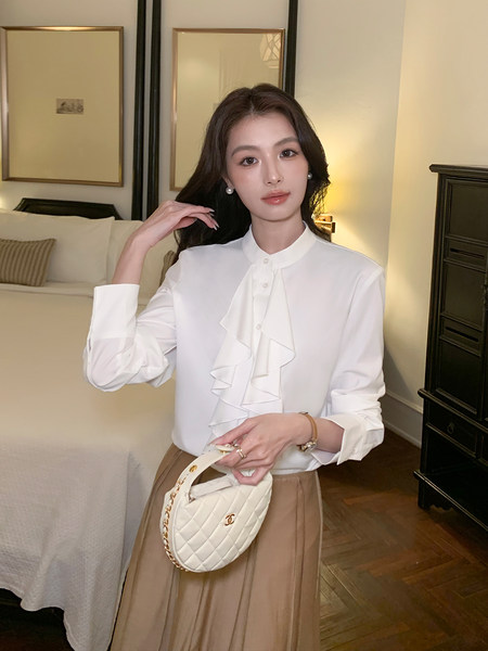 Woman wearing a white ruffled blouse and holding a quilted cream handbag