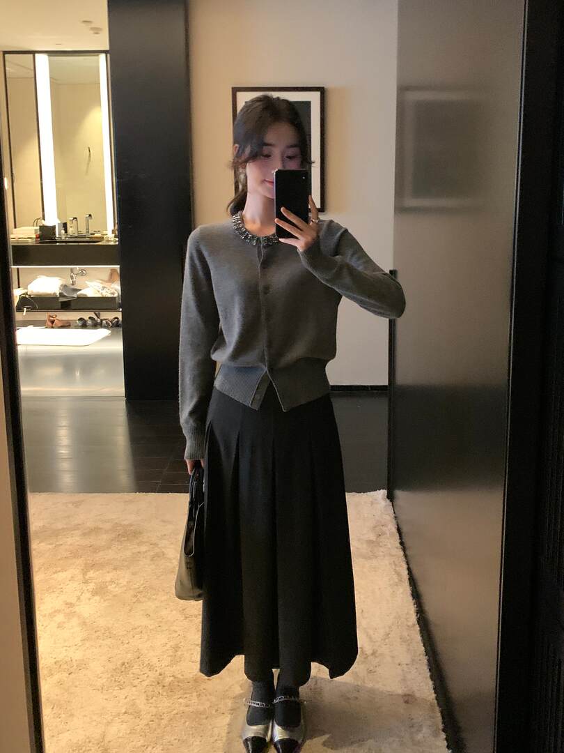 Woman wearing a gray embellished cardigan with a black pleated skirt in a mirror selfie