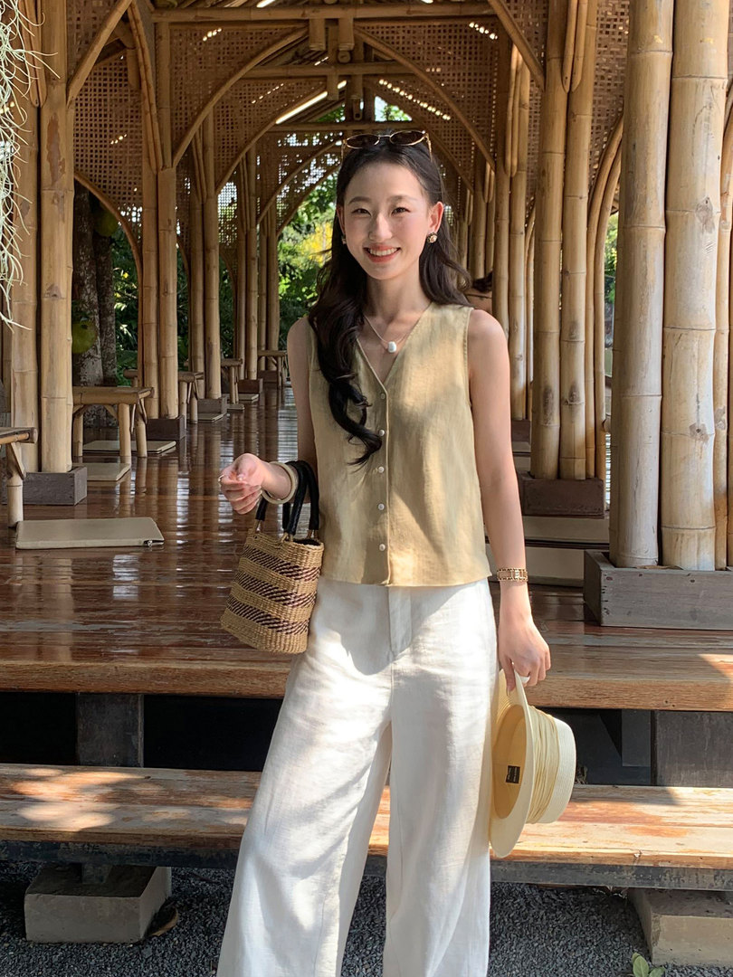 Woman wearing a sleeveless beige button-front top with white wide-leg pants and woven accessories