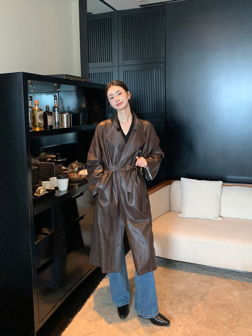 Woman wearing a brown leather trench coat over jeans