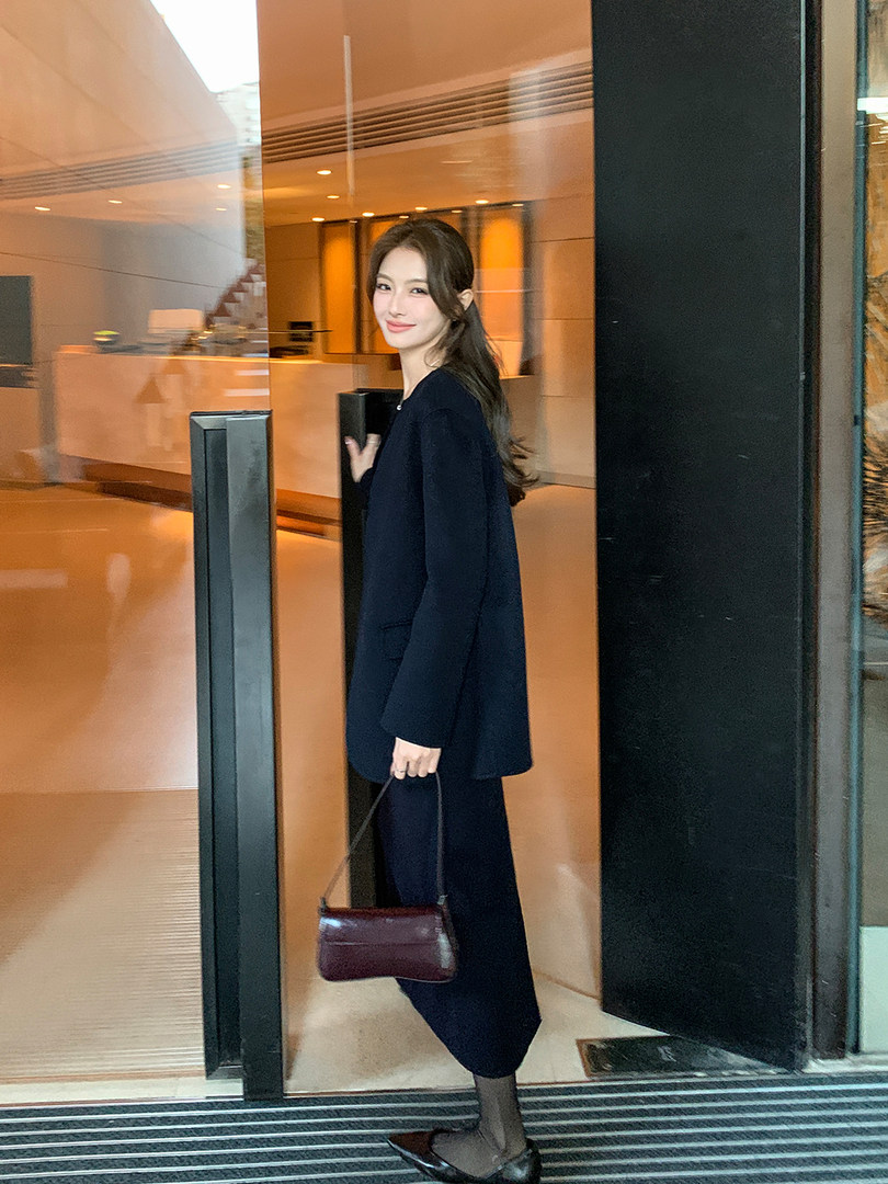 Woman modeling a dark tailored outfit and carrying a small handbag