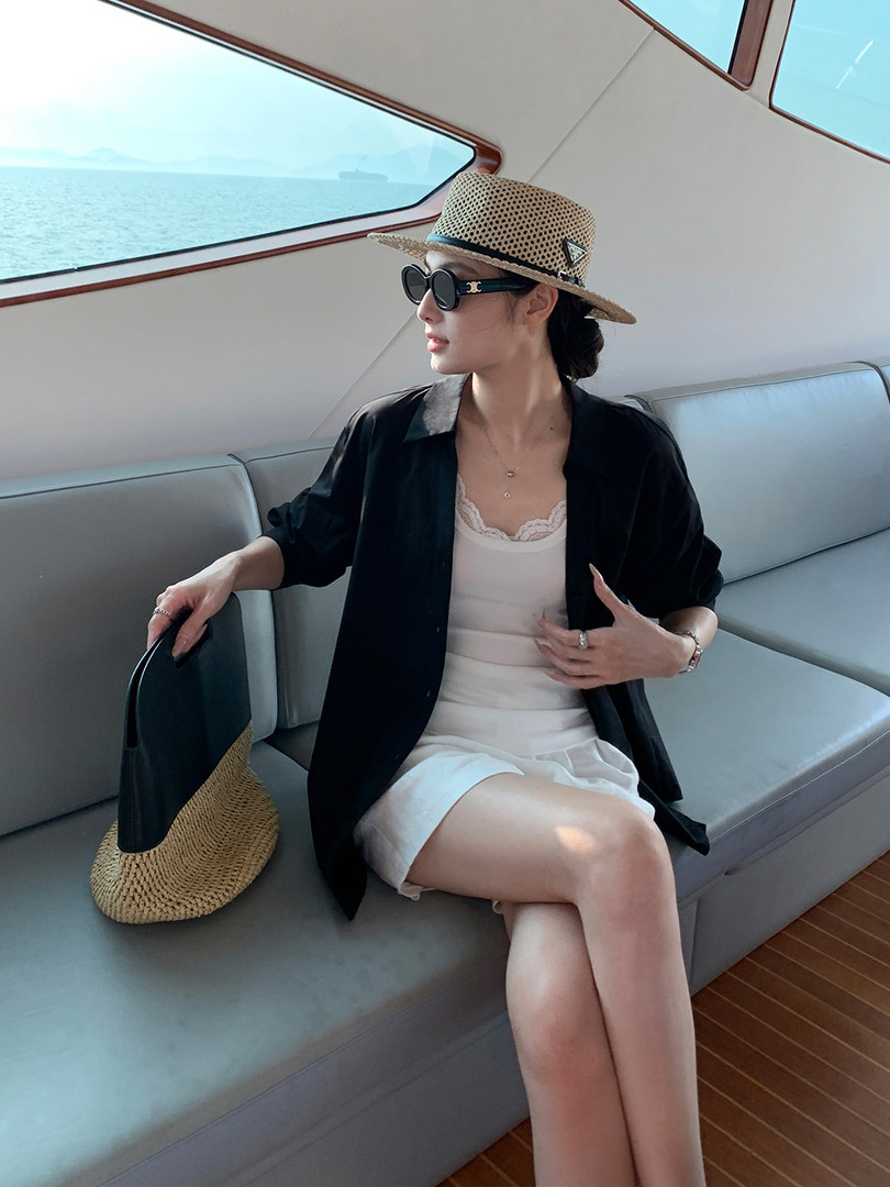 Woman wearing a black cover-up, white dress, straw hat, and sunglasses on a boat