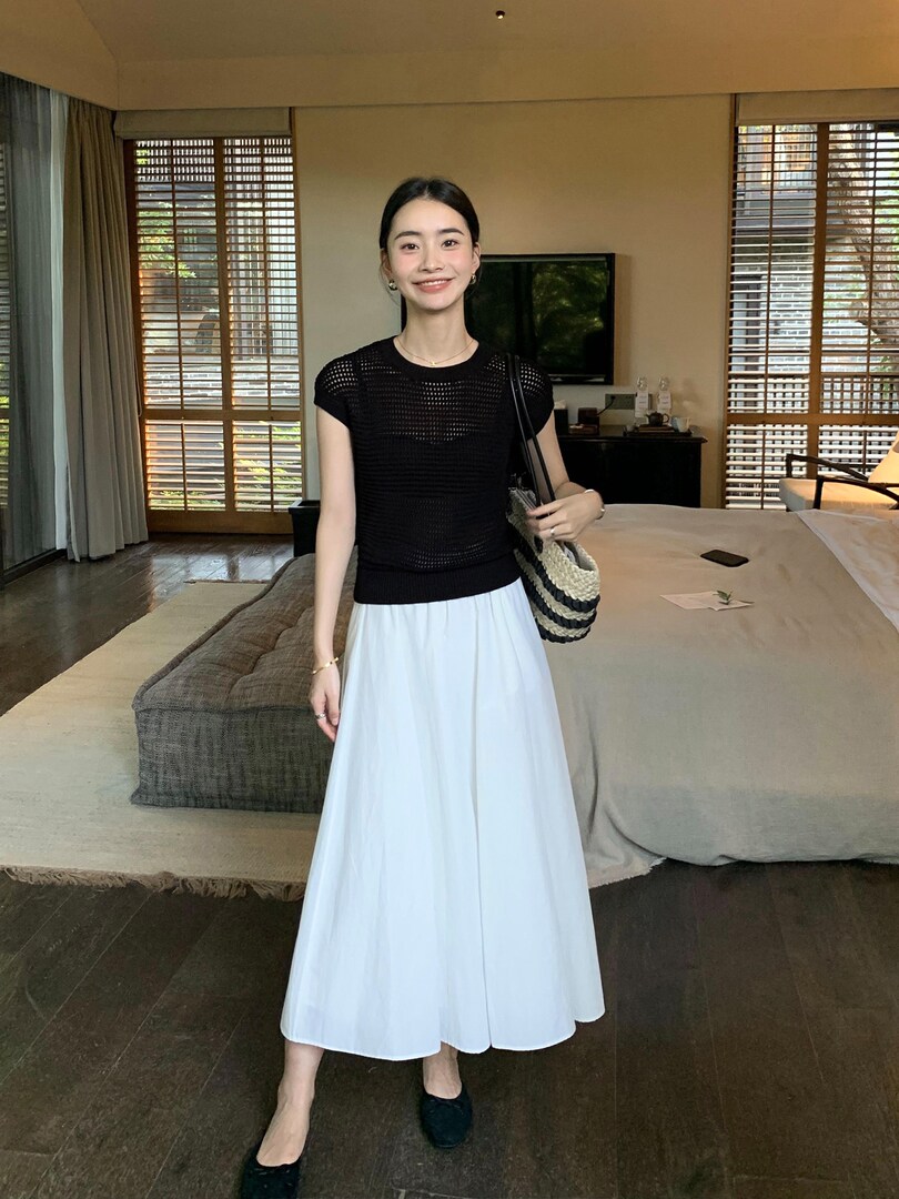 Woman modeling a black short-sleeve top with a white midi skirt and black flats