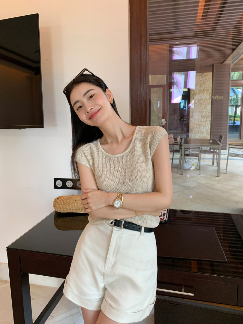 Woman wearing a beige sleeveless knit top with white shorts